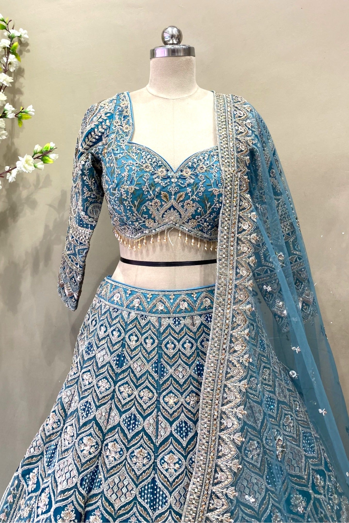 Close-up of a premium designer teal lehenga blouse showcasing a sweetheart neckline, three-quarter sleeves, heavy zardosi embroidery, and beaded fringe tassels.