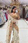 Full-length view of a woman wearing a luxury ivory silk saree with heavy multi-colored peacock hand-embroidery and floral zari borders at Urban Dulhaniya Pune.