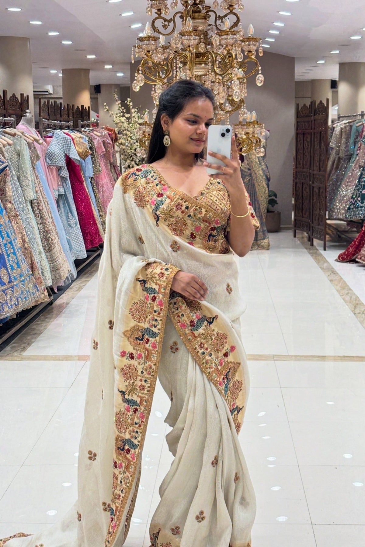 Full-length view of a woman wearing a luxury ivory silk saree with heavy multi-colored peacock hand-embroidery and floral zari borders at Urban Dulhaniya Pune.