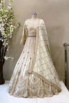 Full view of luxury ivory bridal lehenga with heavy gold embroidery and scalloped hem on display at Urban Dulhaniya.