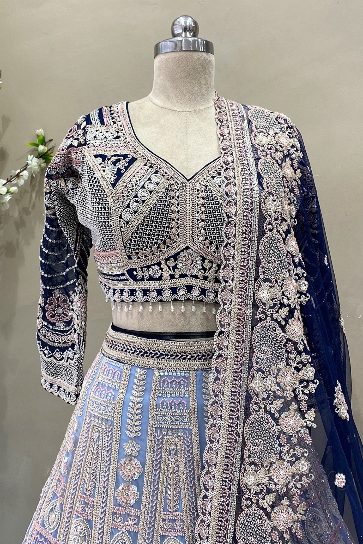 Close-up detail of a designer midnight blue V-neck lehenga blouse with long sleeves, heavy silver embroidery, and crystal drop tassels.