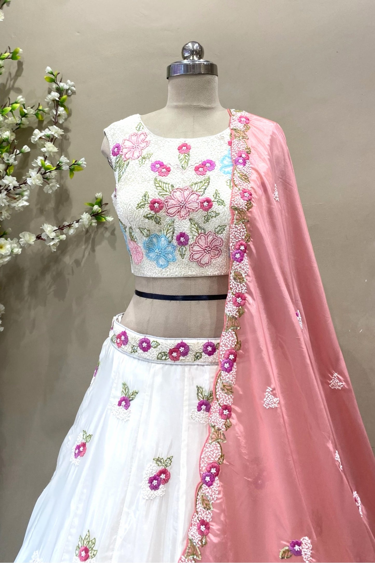 Close-up of a premium ivory sleeveless lehenga blouse showcasing intricate pink and blue floral threadwork embroidery, perfect for day weddings.