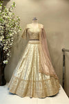Full front view of a luxury ivory raw silk bridal lehenga with heavy gold zardosi embroidery and a peach scalloped dupatta at Urban Dulhaniya Pune.
