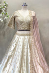 Close-up of a designer ivory V-neck lehenga blouse with heavy gold handwork and crystal drop tassels for a bridal trousseau.