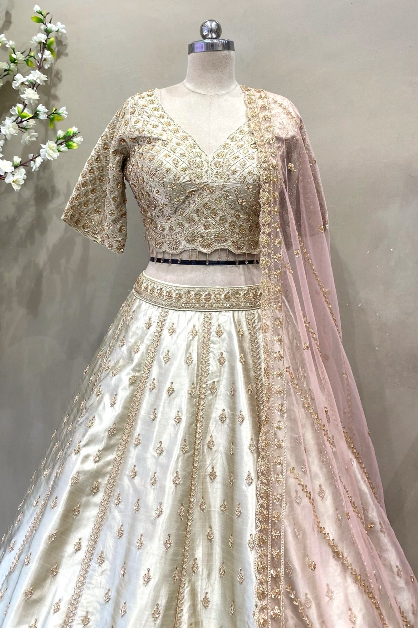 Close-up of a designer ivory V-neck lehenga blouse with heavy gold handwork and crystal drop tassels for a bridal trousseau.