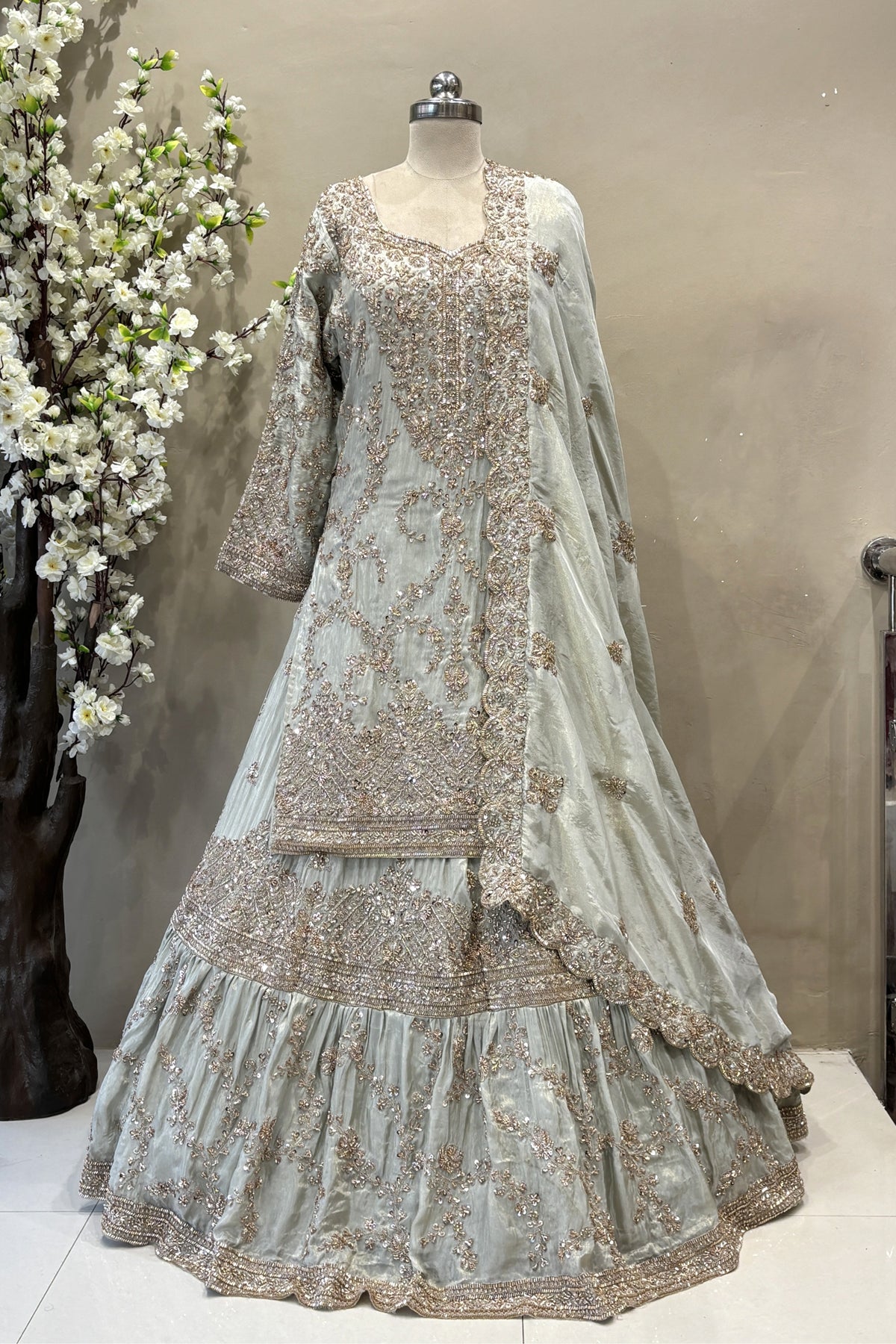 Close-up of a designer long-sleeve bridal blouse with sheer sleeves, crystal fringe tassels, and intricate pink floral beadwork.