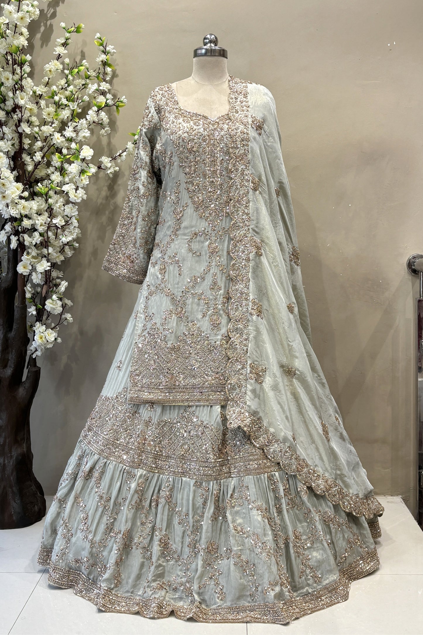 Close-up of a designer long-sleeve bridal blouse with sheer sleeves, crystal fringe tassels, and intricate pink floral beadwork.
