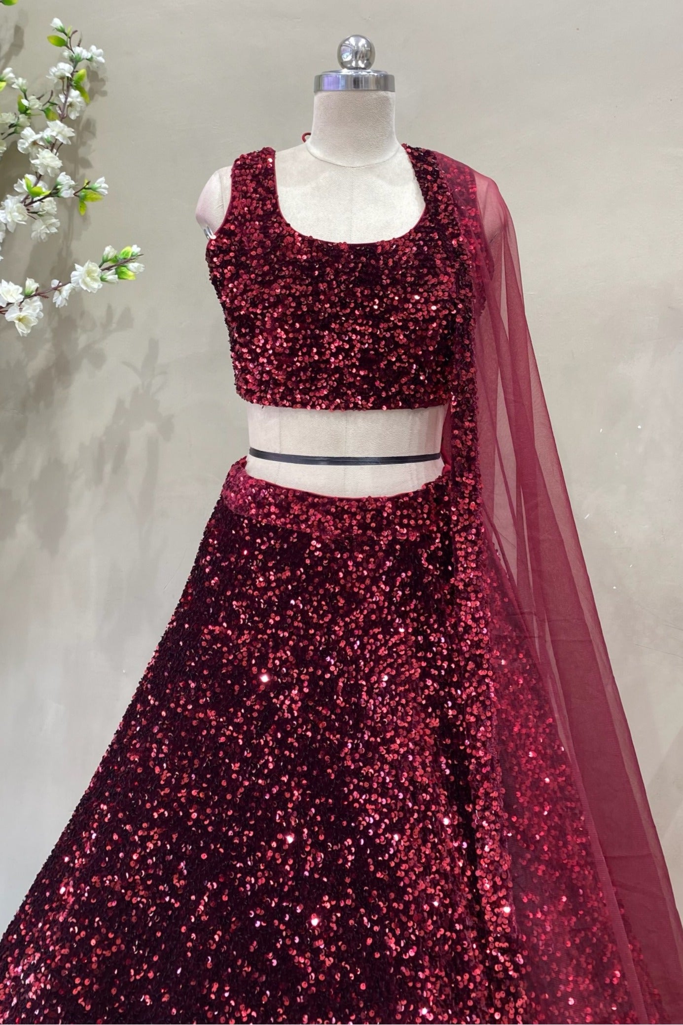 Close-up of a designer maroon sequin sleeveless lehenga blouse with a scoop neckline, paired with a sheer net dupatta for cocktail parties.