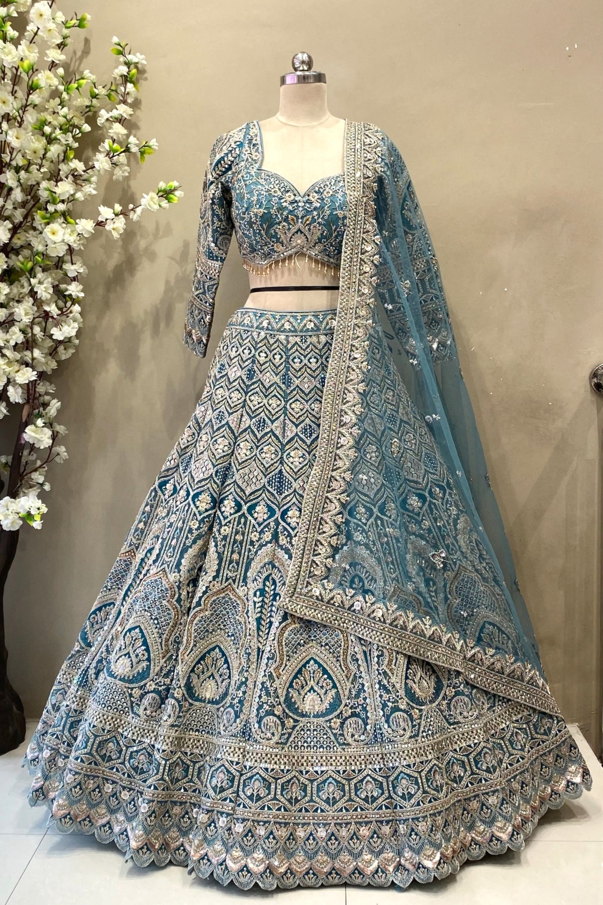 Detail shot highlighting the dense geometric sequin and crystal beadwork on a flared teal blue reception lehenga skirt.