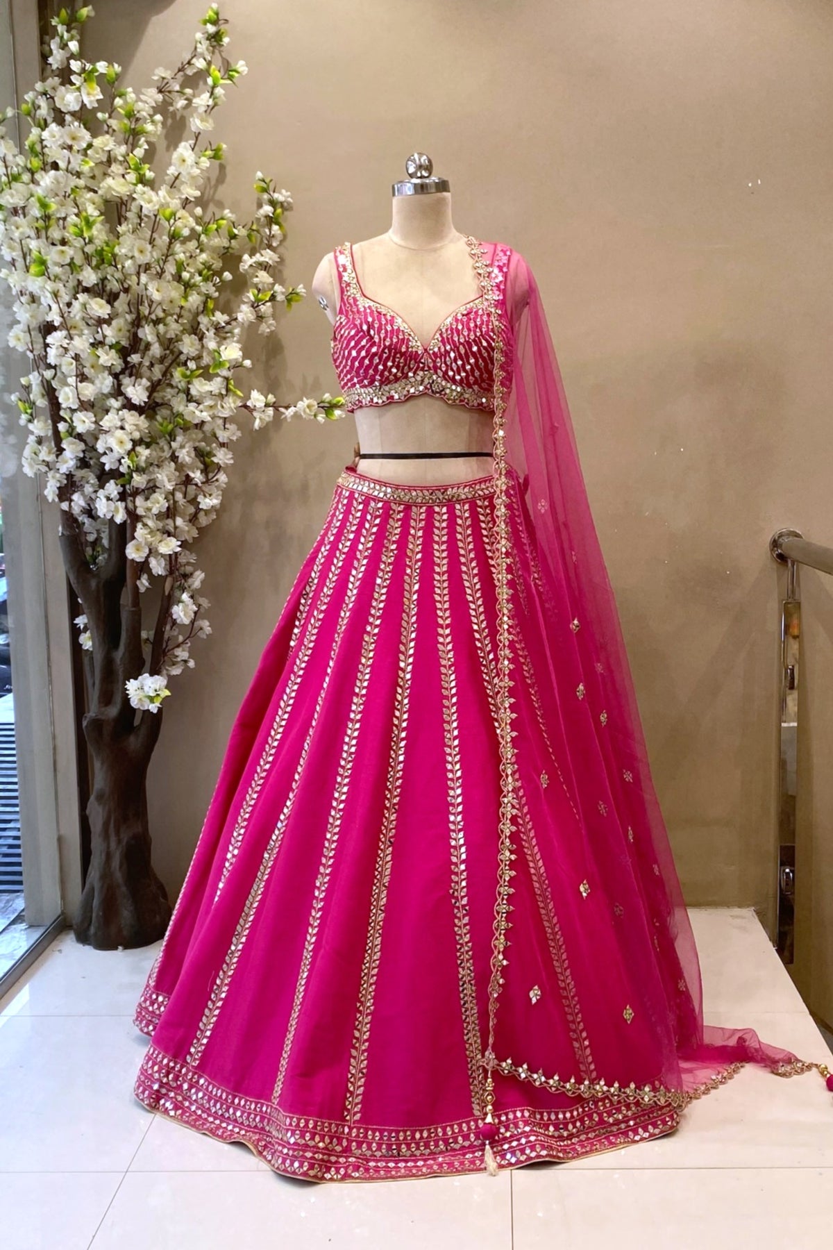 Full-length view of a vibrant Rani Pink mirror lehenga with vertical leaf motifs and a sweetheart neck blouse at Urban Dulhaniya Pune.