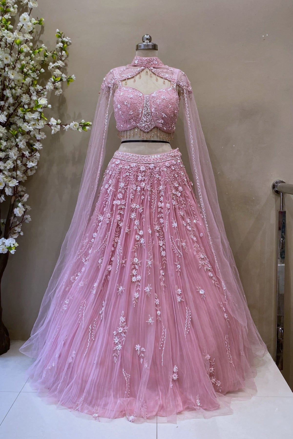 Full-length view of a blush pink 3D floral Indo-western gown with sheer cape sleeves and a choker neck at Urban Dulhaniya Pune.