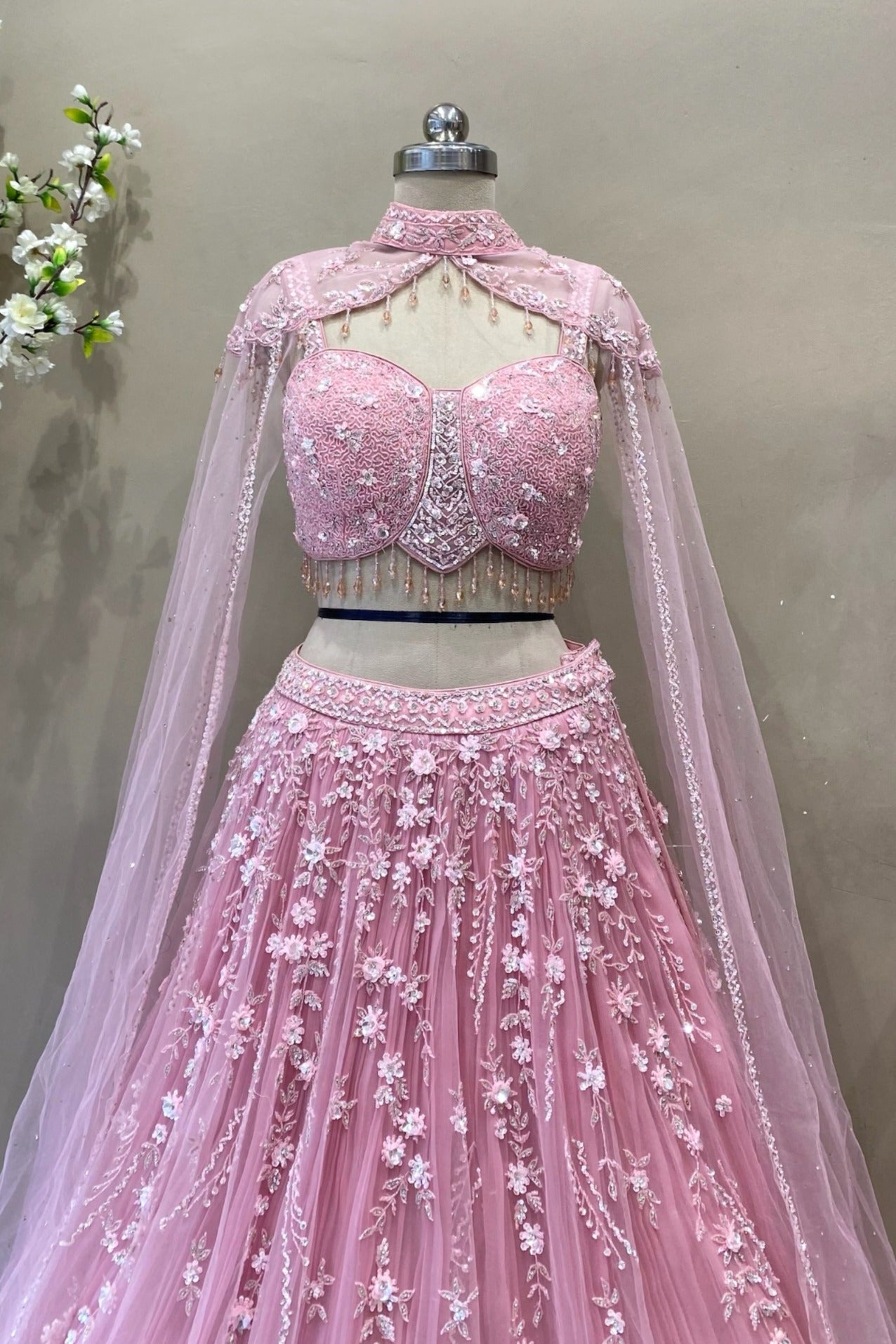 Close-up of a luxury pink corset bodice with crystal beadwork, fringe hem, and sheer cape sleeves for a reception look.