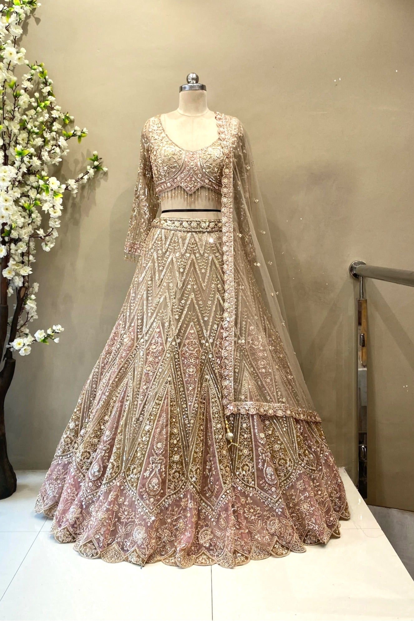 Full-length view of a luxury champagne pink heavy beads work bridal lehenga with a zig-zag pattern and long-sleeve blouse at Urban Dulhaniya.