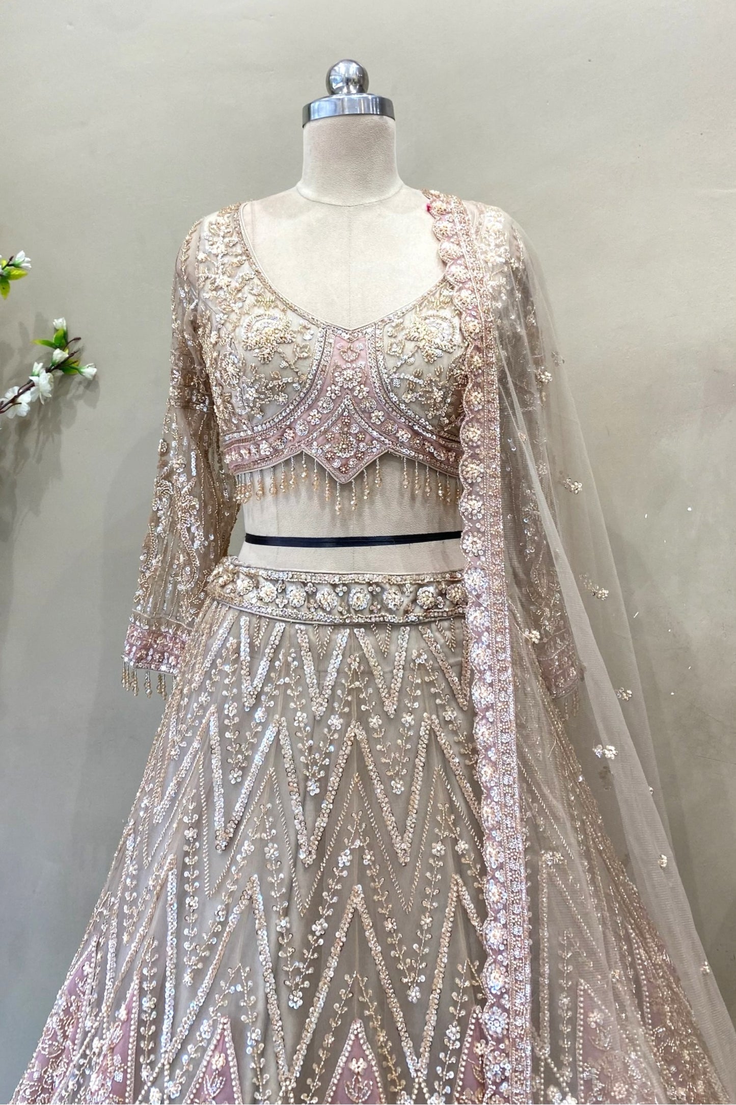 Close-up of a designer long-sleeve bridal blouse with sheer sleeves, crystal fringe tassels, and intricate pink floral beadwork.