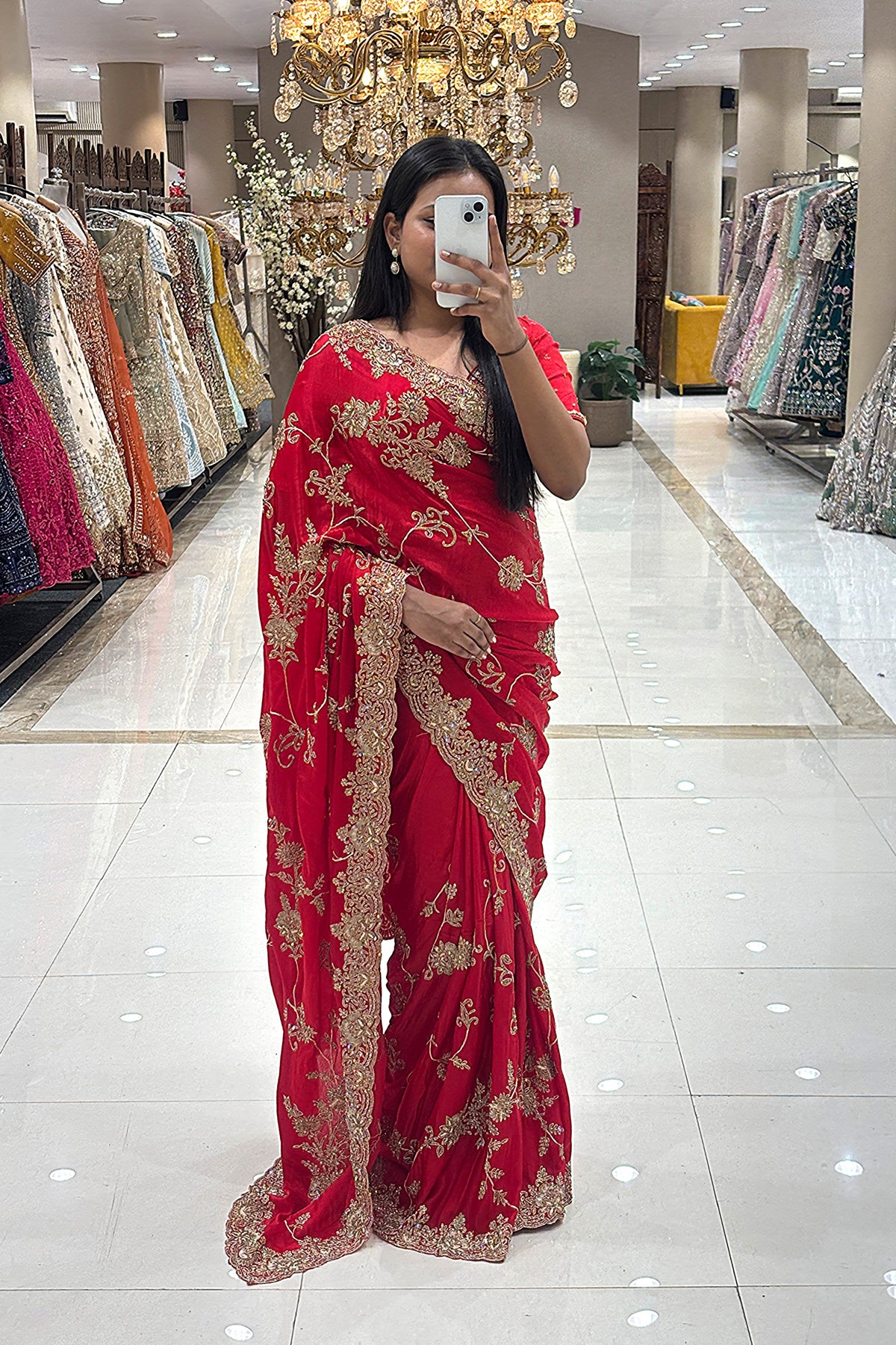 Full-length view of a woman taking a mirror selfie wearing a luxury classic red pure handwork designer saree with heavy gold floral borders, showcased at the Urban Dulhaniya boutique in Pune