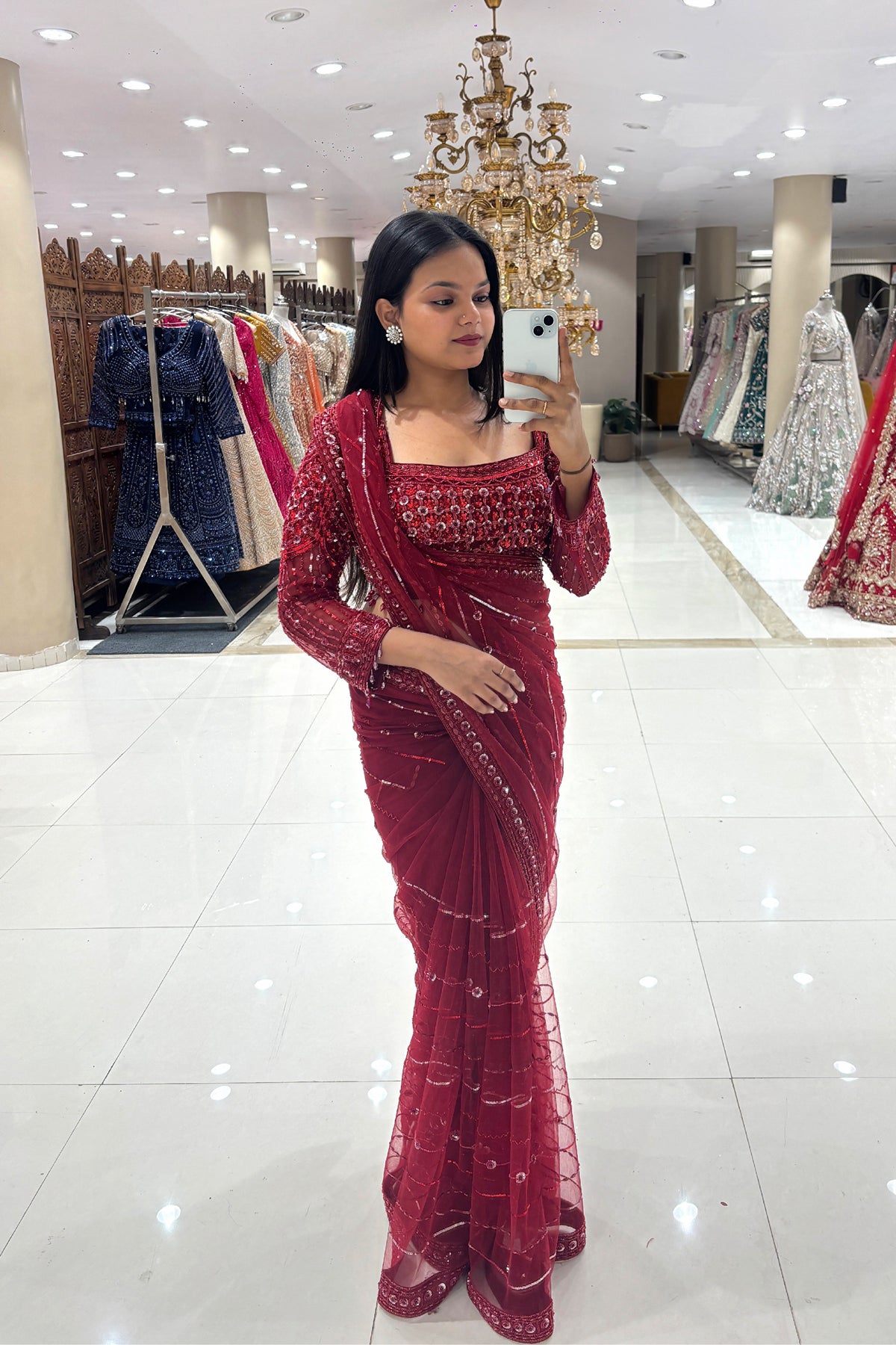 Full-length mirror selfie of a woman wearing a luxury ruby red pure handwork sequin cocktail saree with a long-sleeve blouse at Urban Dulhaniya boutique in Pune.