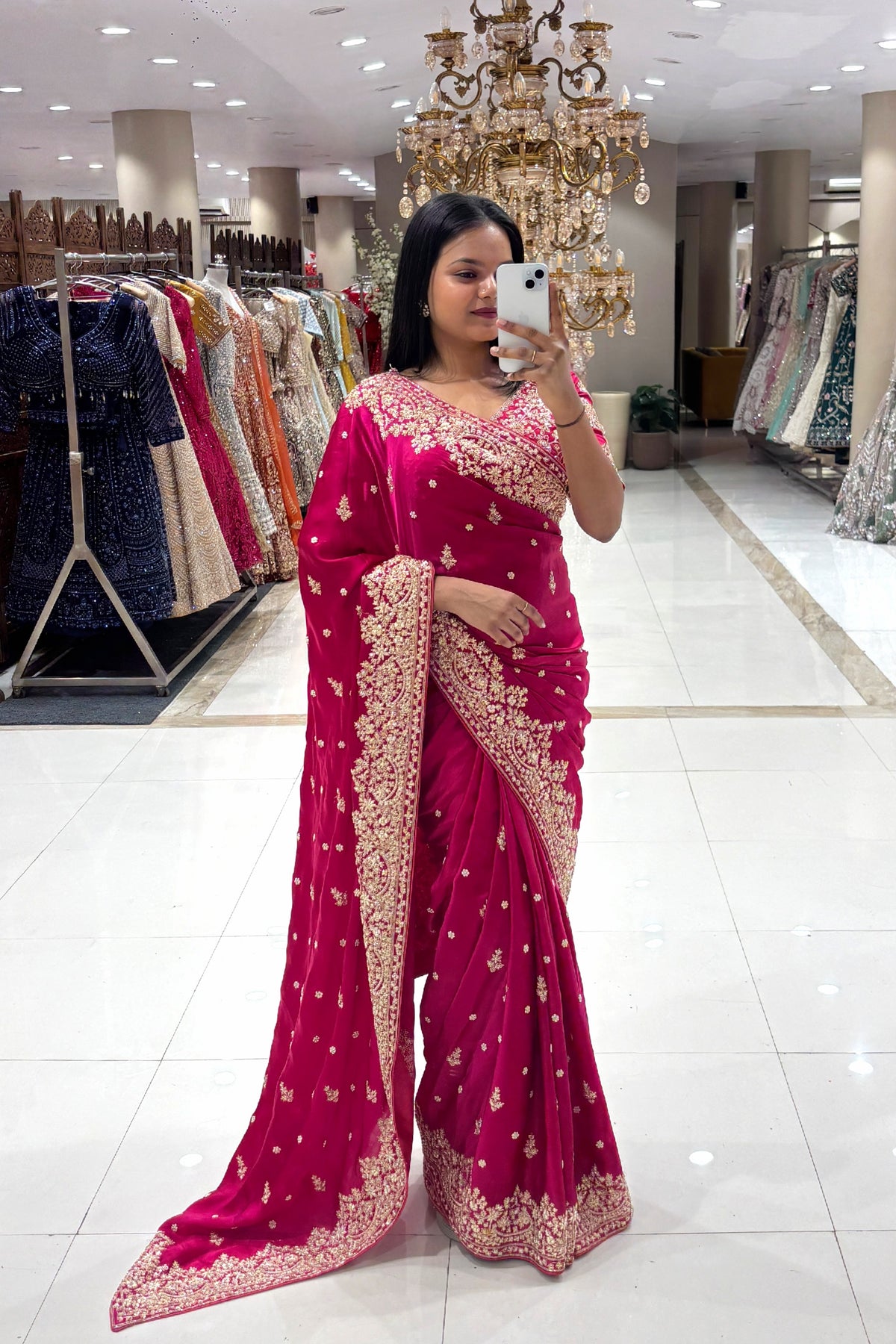 Full-length view of a woman taking a mirror selfie wearing a luxury hot pink pure handwork designer saree with heavy gold floral borders at the Urban Dulhaniya boutique in Pune.