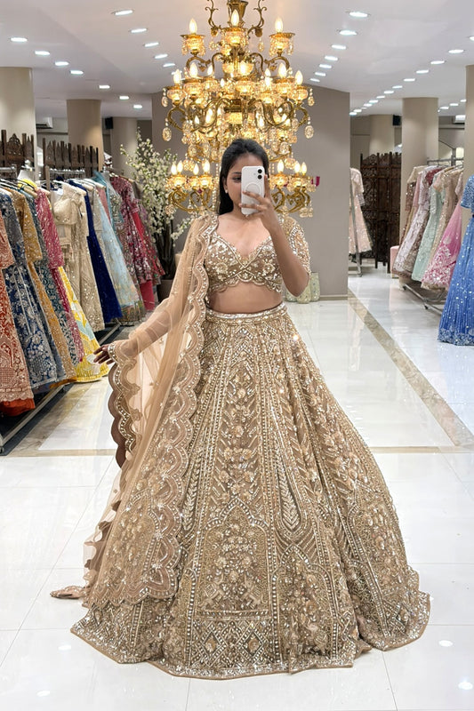 Full-length mirror selfie of a bride wearing a luxury champagne gold heavy handwork bridal lehenga with a scalloped dupatta at the Urban Dulhaniya boutique.