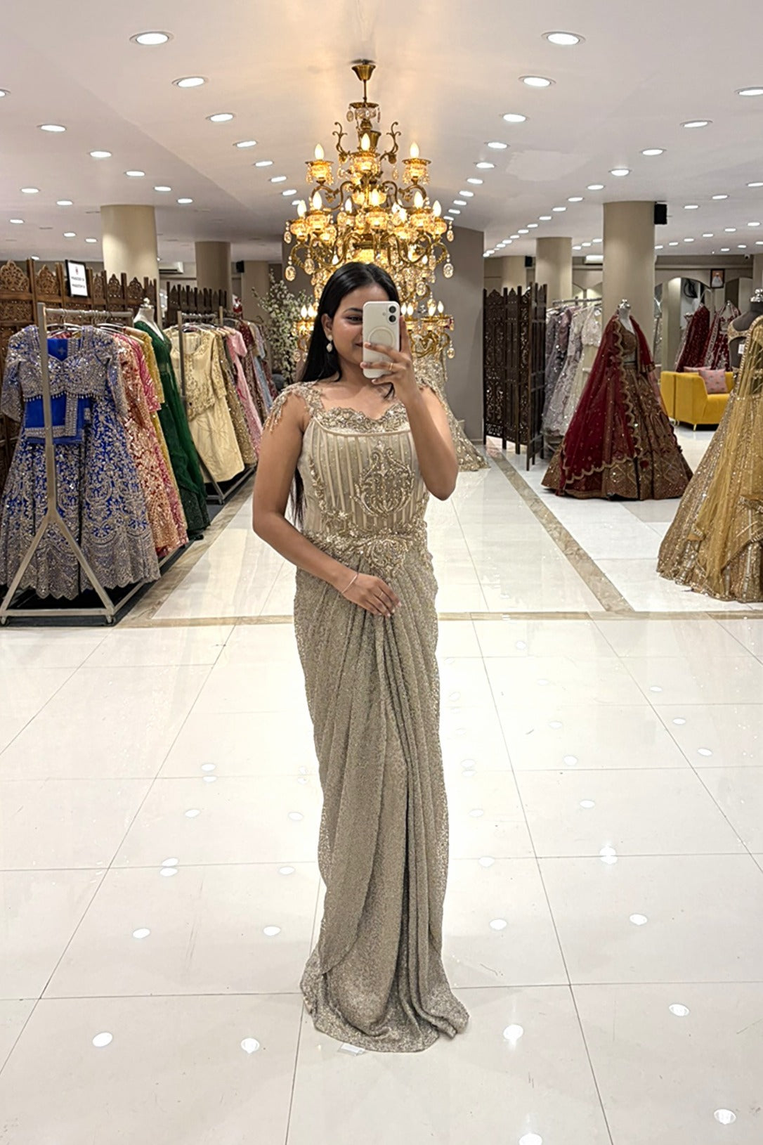 Full-length view of a woman taking a mirror selfie wearing a luxury metallic silver draped Indo-Western gown with a heavy handwork corset bodice at the Urban Dulhaniya boutique in Pune.