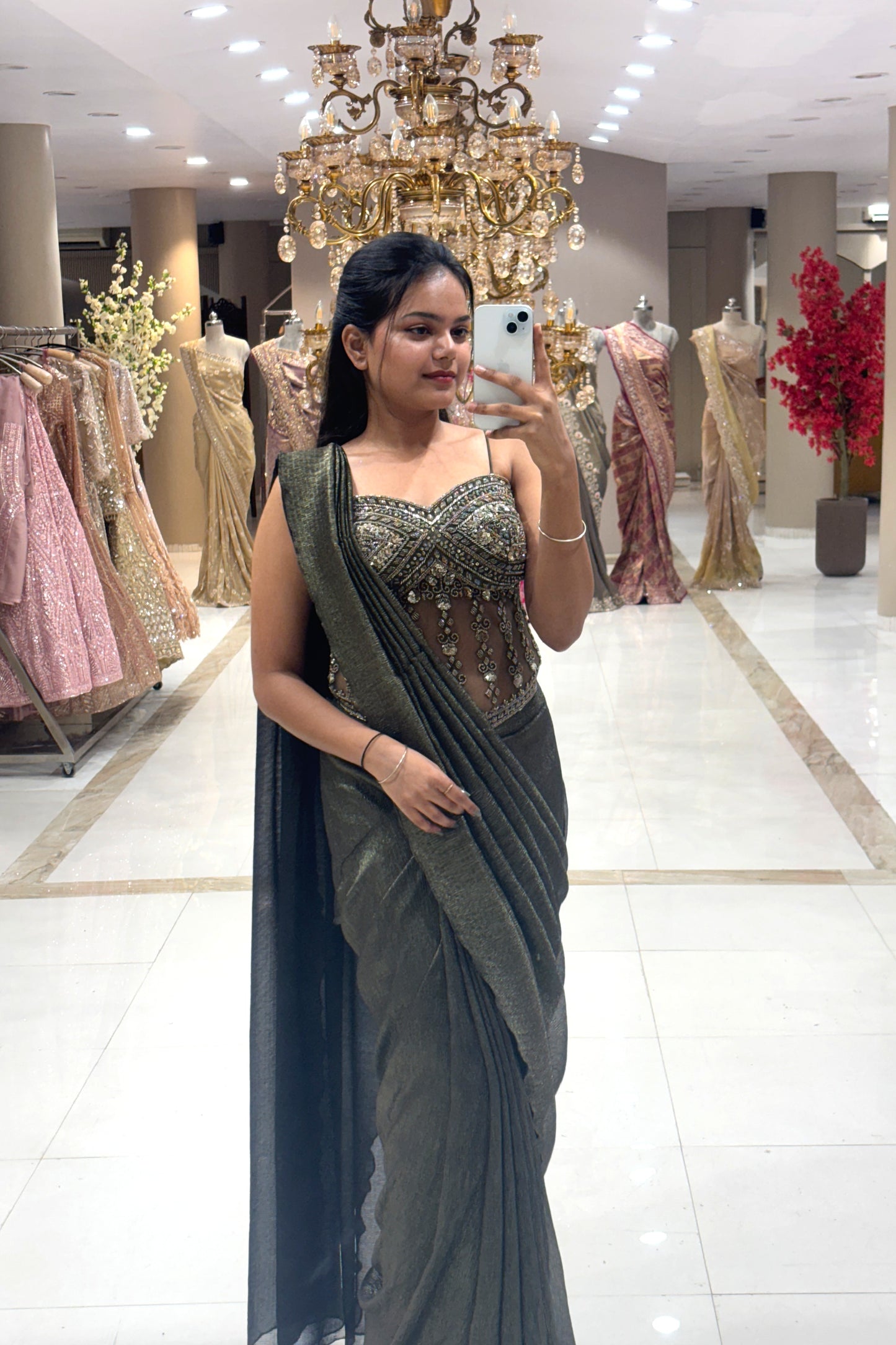 Full-length mirror selfie of a woman wearing a luxury metallic olive pre-draped Indo-Western saree with a heavy handwork sheer corset blouse at the Urban Dulhaniya boutique.