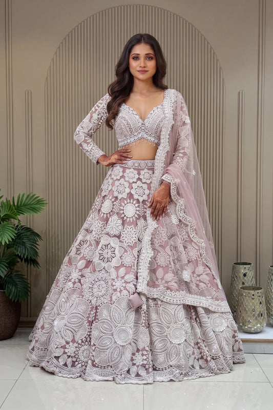 Mauve lavender designer lehenga with ivory pearlwork and cutdana floral embroidery, featuring a V-neck blouse and scalloped net dupatta against a fluted wall background.