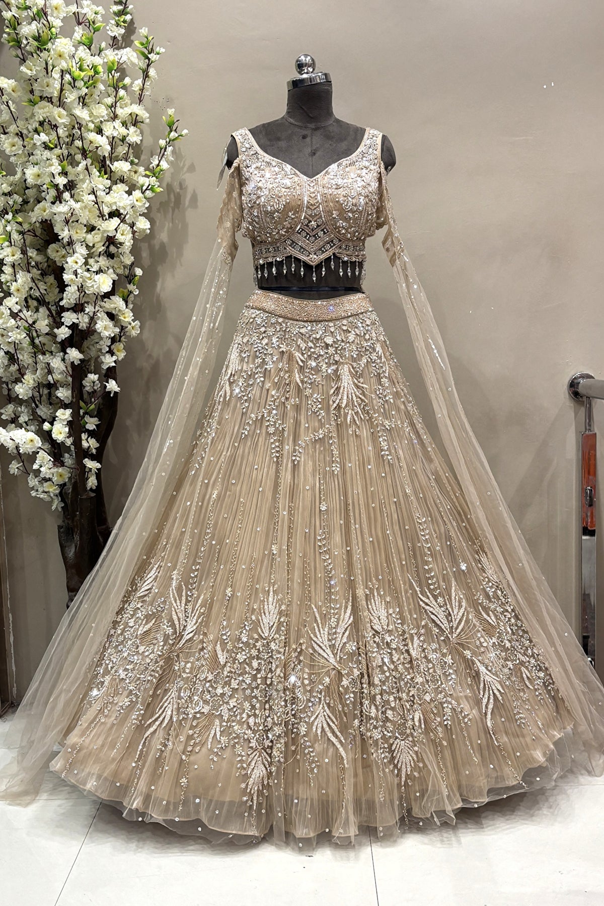 Full-length view of a luxury silver crystal embellished designer bridal lehenga with sheer long sleeves displayed on a mannequin at the Urban Dulhaniya boutique.