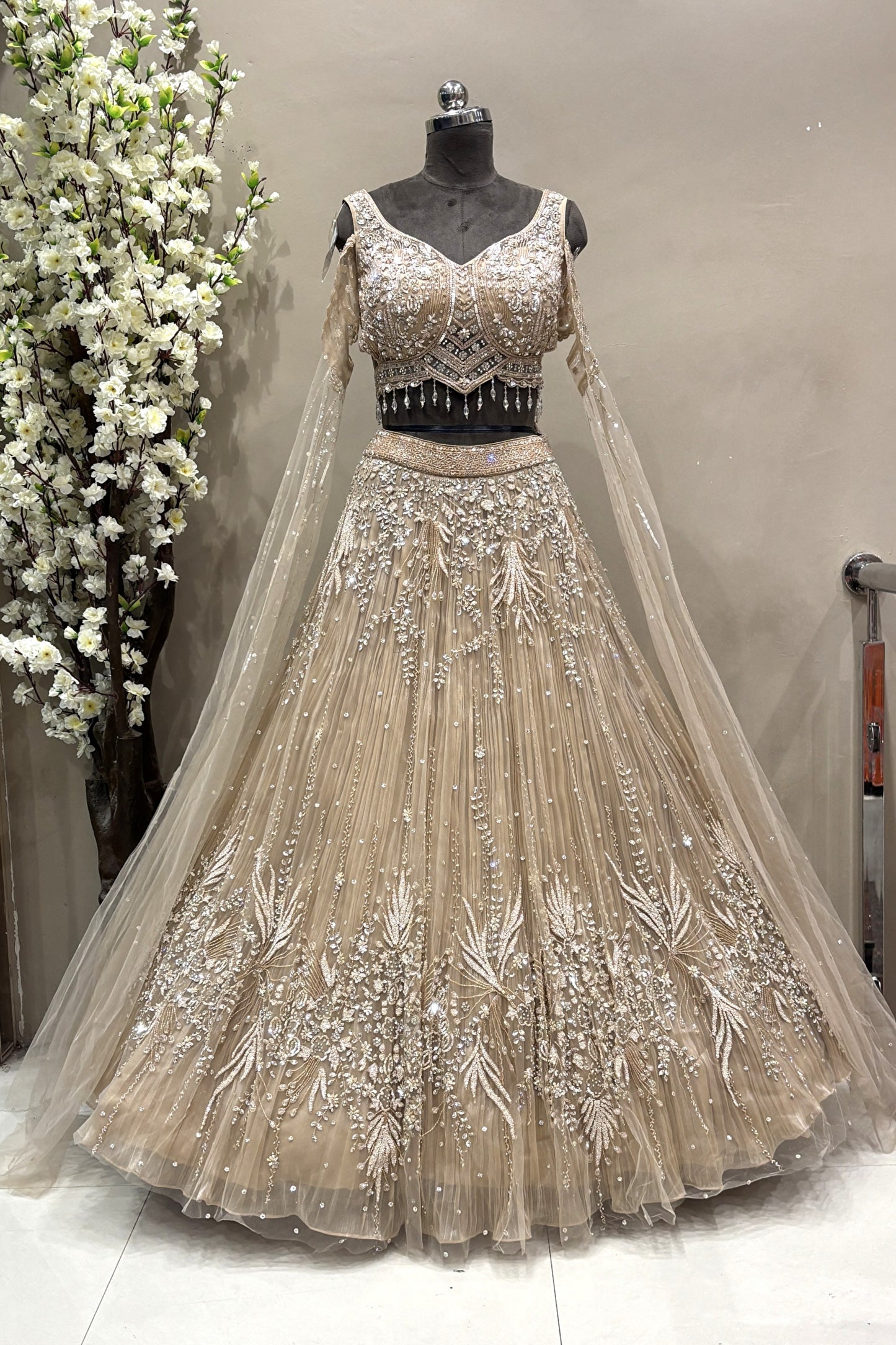 Full-length view of a luxury silver crystal embellished designer bridal lehenga with sheer long sleeves displayed on a mannequin at the Urban Dulhaniya boutique.