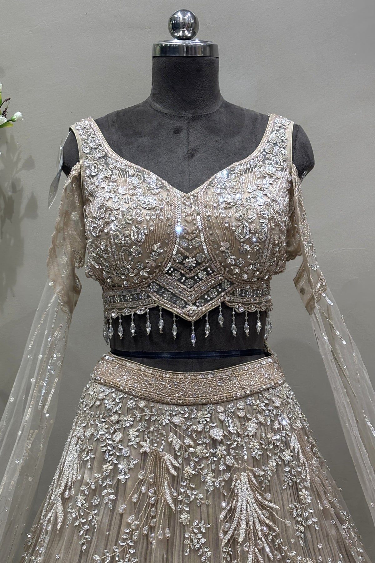 Close-up of a designer silver V-neck lehenga blouse featuring heavy crystal embroidery, cold-shoulder sleeves, and beaded fringe tassels.