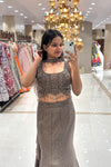 Close-up of a designer taupe bronze lehenga blouse featuring intricate handwork, an attached embellished choker, and beaded hem tassels for cocktail parties.